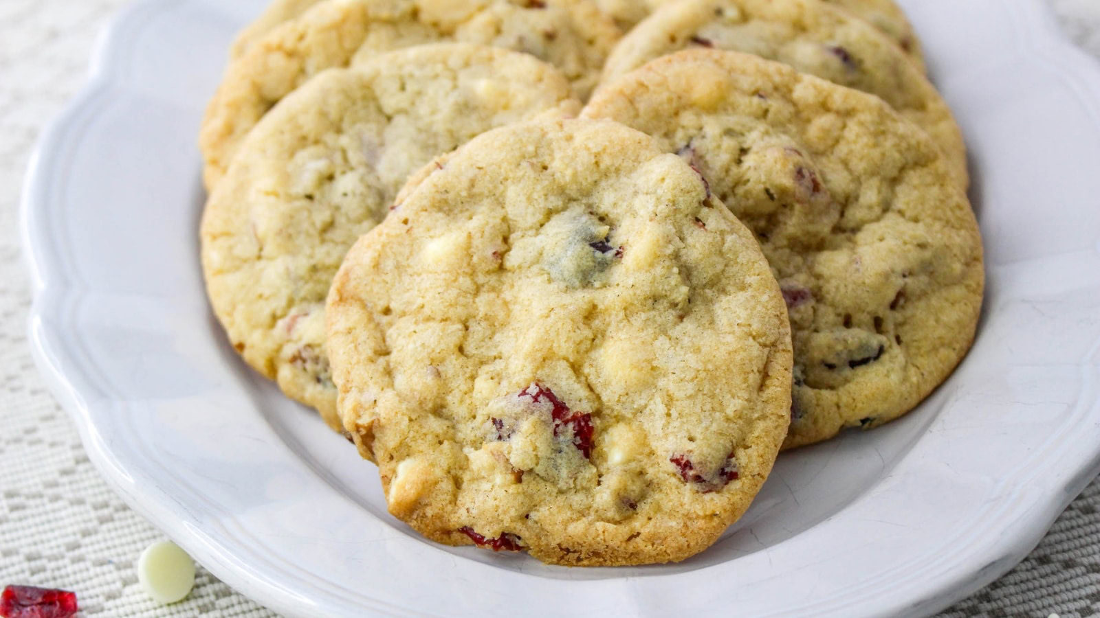 A white plate with several white chocolate and cranberry cookies arranged in a slightly overlapping manner.