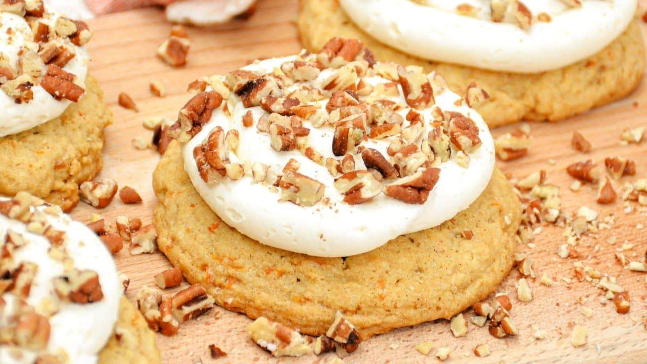A close-up of frosted cookies topped with chopped pecans on a wooden surface.