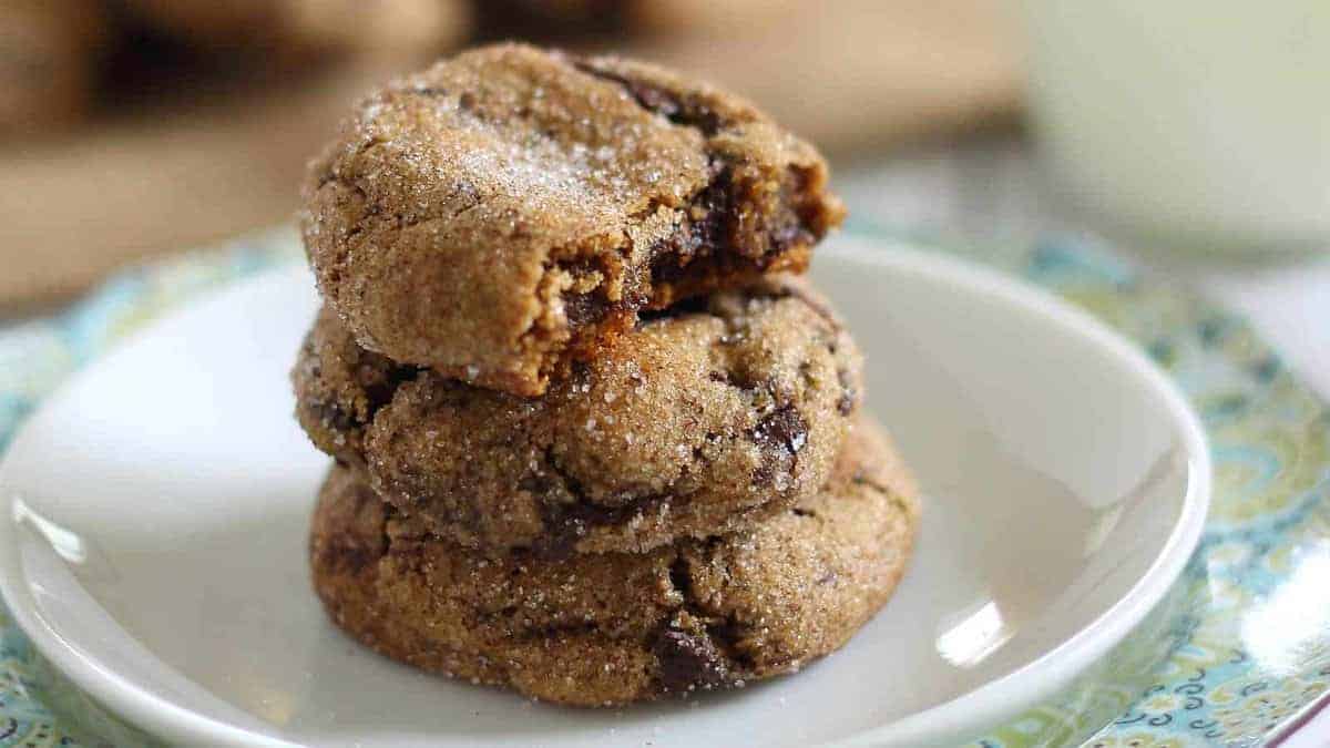 Three sugar-coated chocolate chip cookies are stacked on a white plate, with one cookie showing a bite taken out of it.