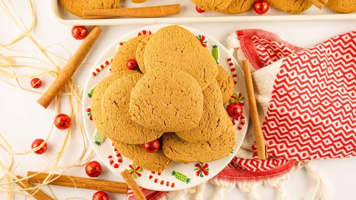 A plate of plain cookies on a decorative dish, surrounded by cinnamon sticks, red ornaments, and a red patterned cloth.