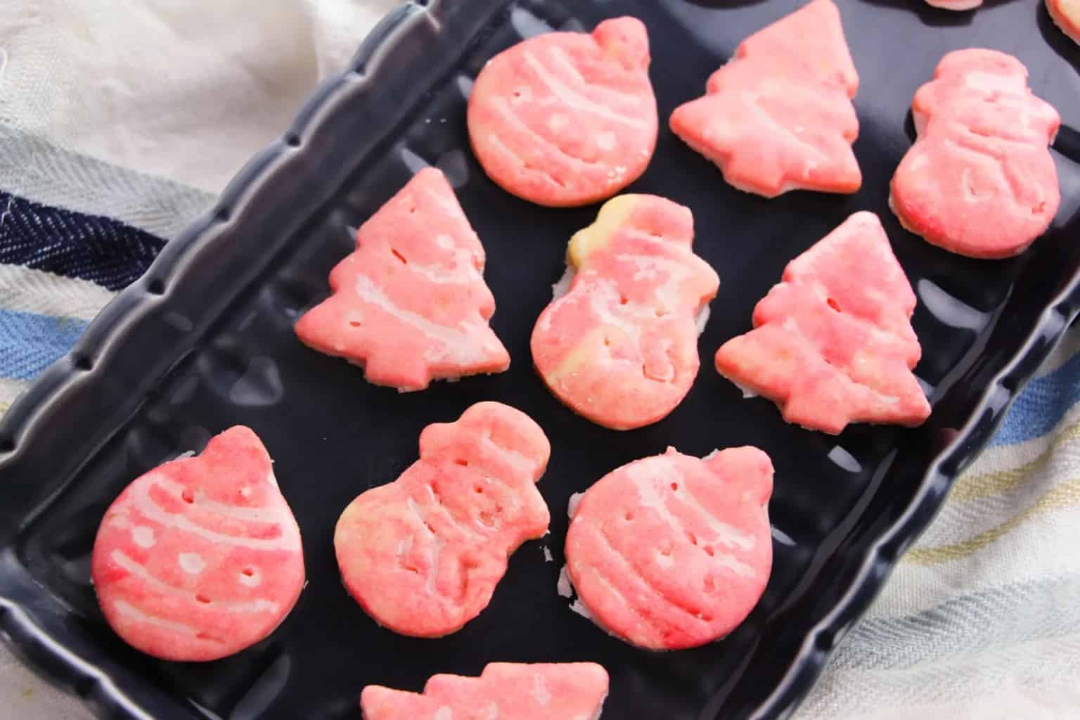 A black tray with pink Christmas-themed cookies shaped like trees, snowmen, and ornaments.