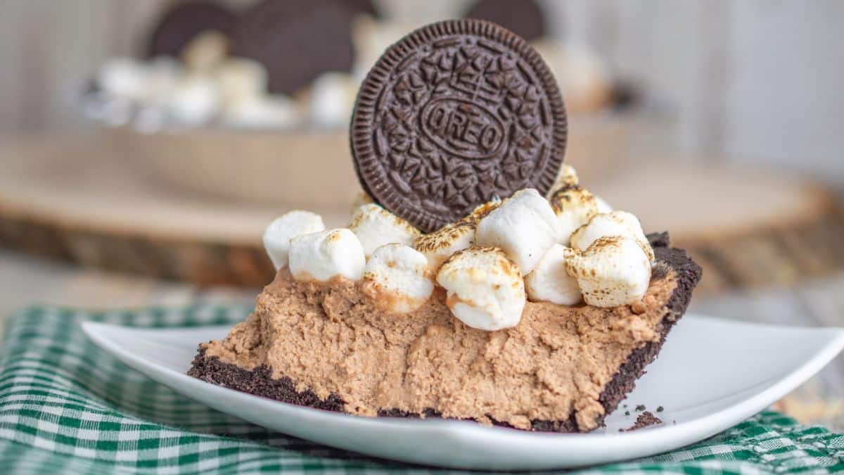 A slice of chocolate pie with an Oreo crust, topped with toasted marshmallows and a whole Oreo cookie, on a white plate.