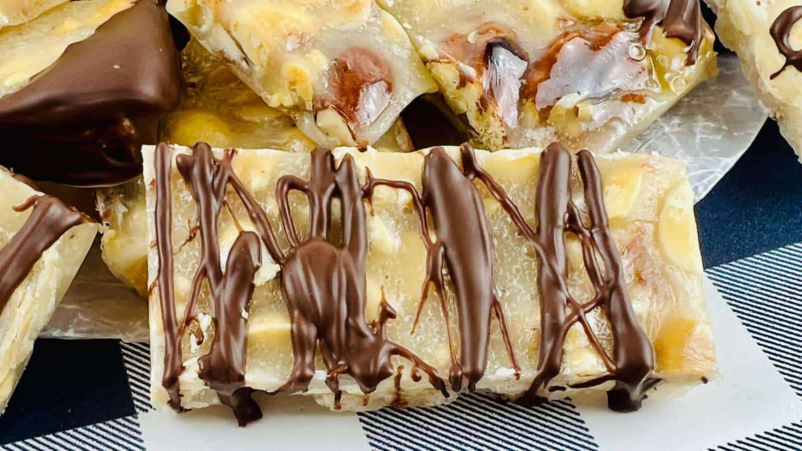 Rectangular candy bars with a marbled appearance are topped with drizzled dark chocolate and displayed on a white and blue checkered surface.