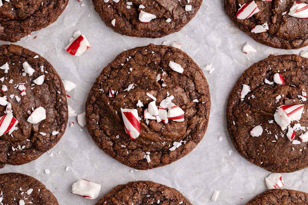 Chocolate cookies topped with crushed peppermint candies arranged on parchment paper.