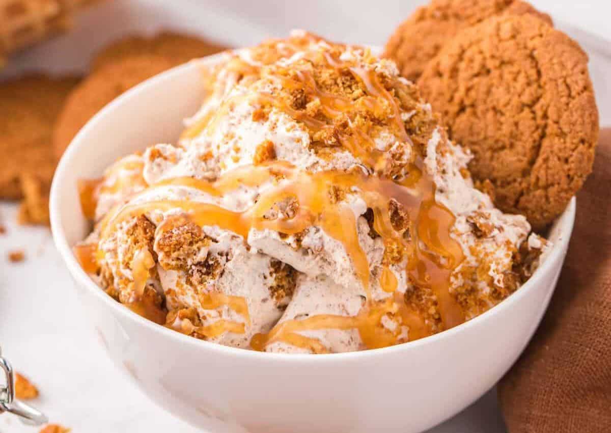 A bowl of ice cream topped with caramel sauce and crumbled cookies, served with two whole cookies on the side.