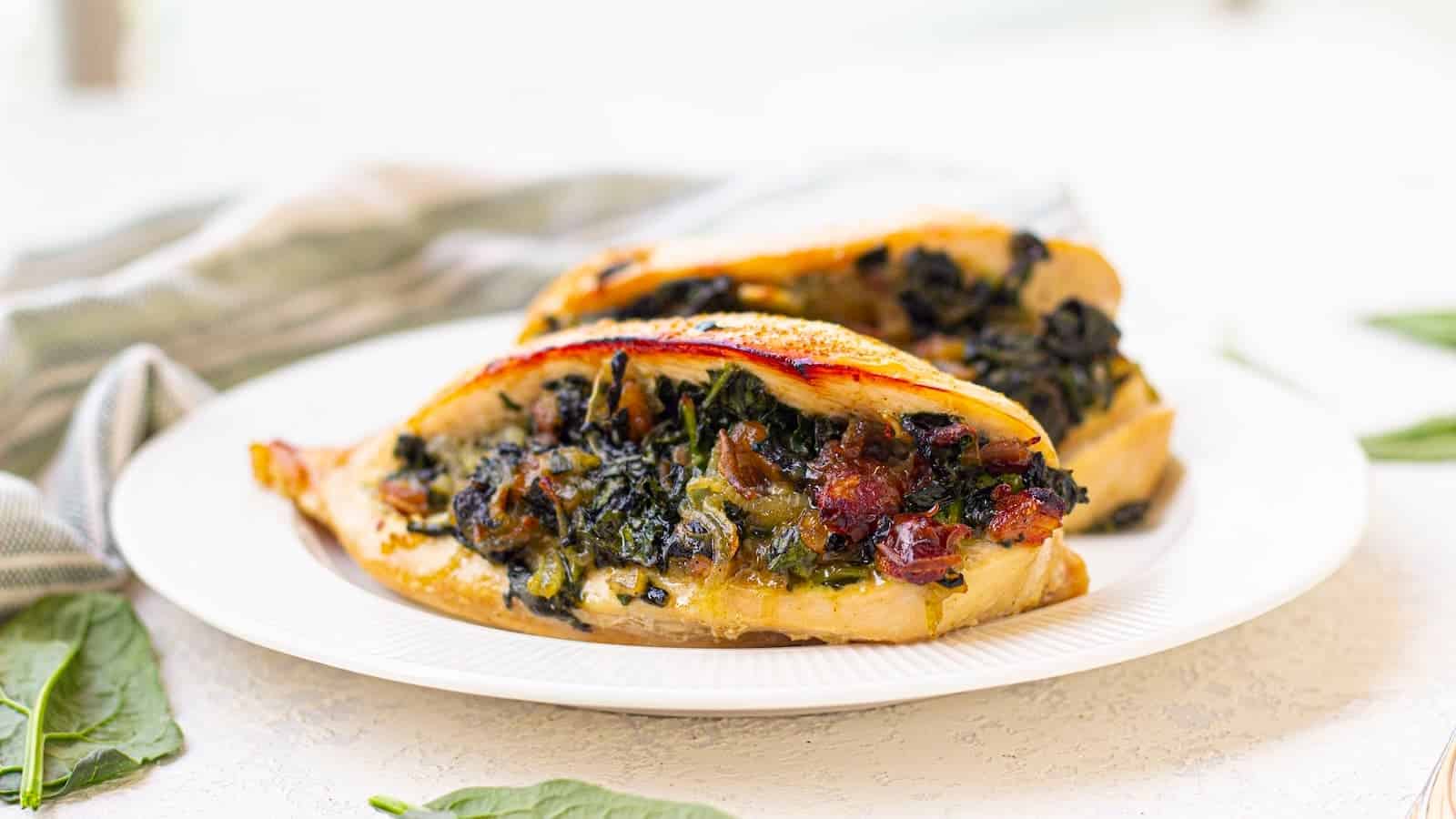 Two pieces of chicken breast stuffed with spinach and sun-dried tomatoes are served on a white plate.