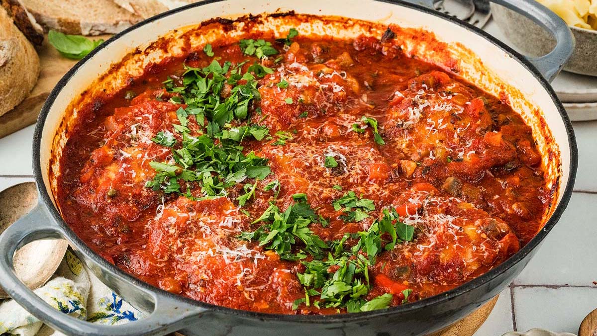 A large pot filled with tomato-based stew featuring several meatballs, topped with grated cheese and fresh chopped parsley.