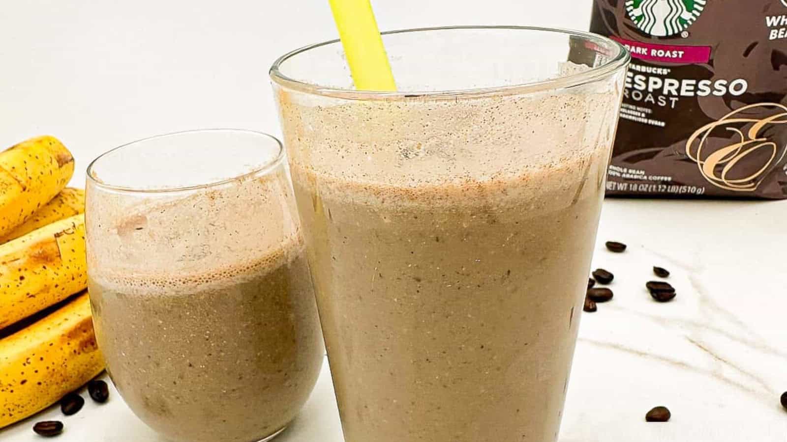 Two glasses of banana coffee smoothie sit on a counter next to a bunch of bananas, coffee beans, and a Starbucks espresso roast bag.