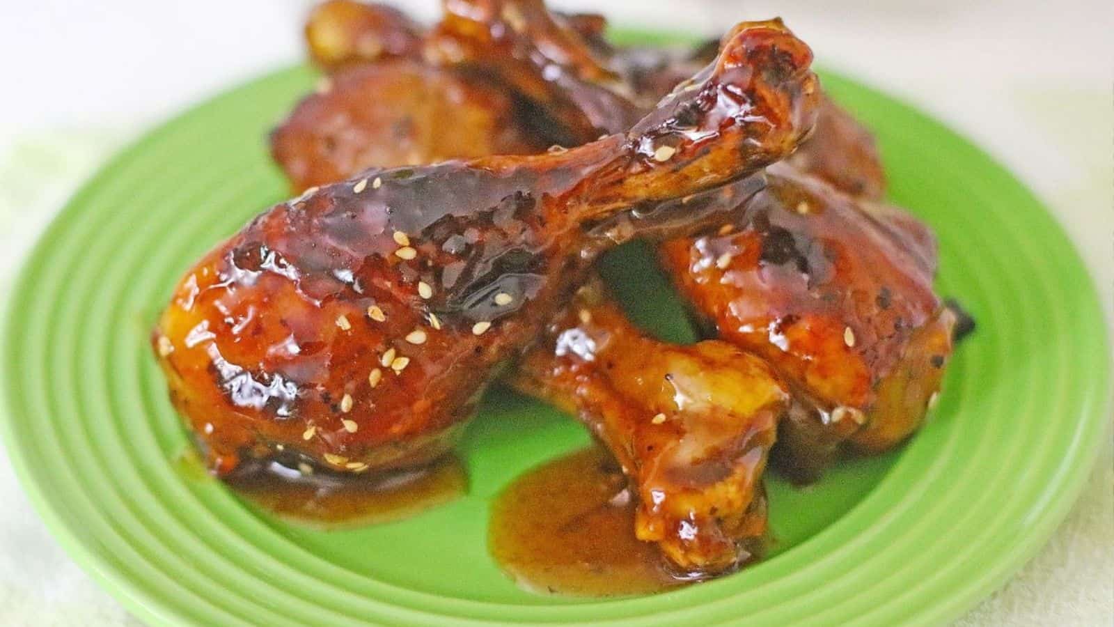 Glazed chicken drumsticks with sesame seeds served on a green plate.