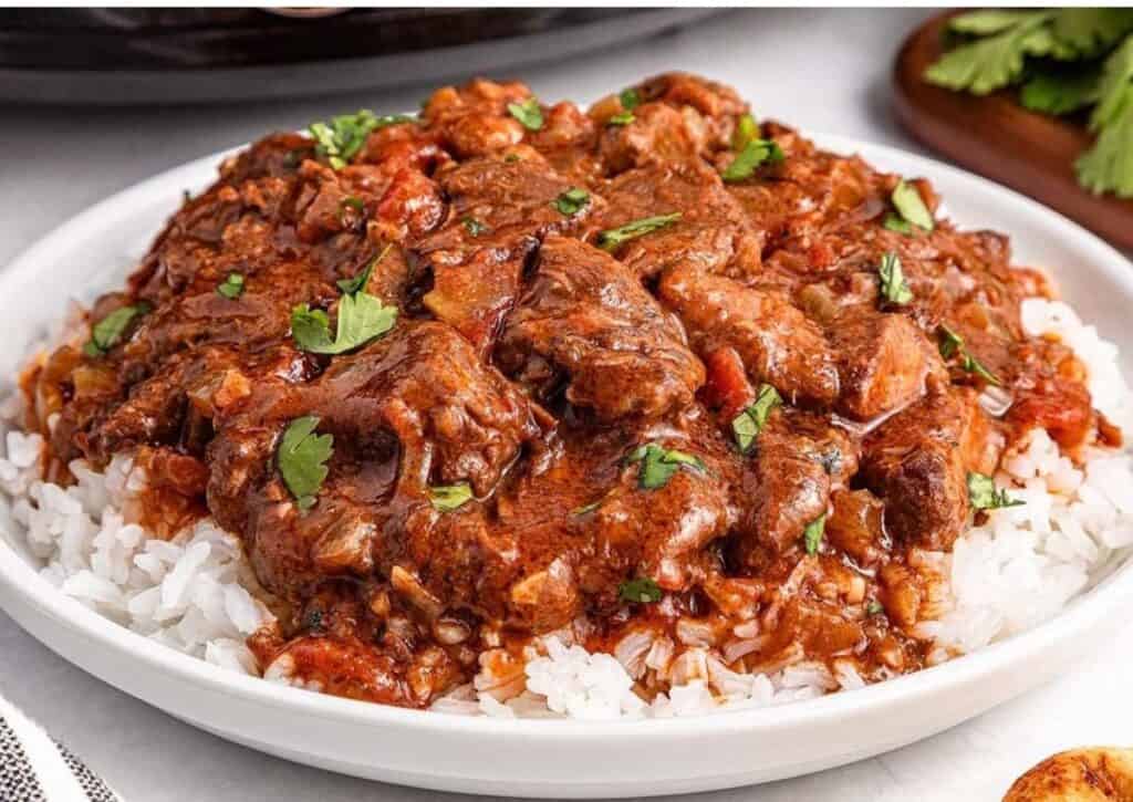 A plate of white rice topped with beef stew in a rich, brown sauce, garnished with chopped parsley.