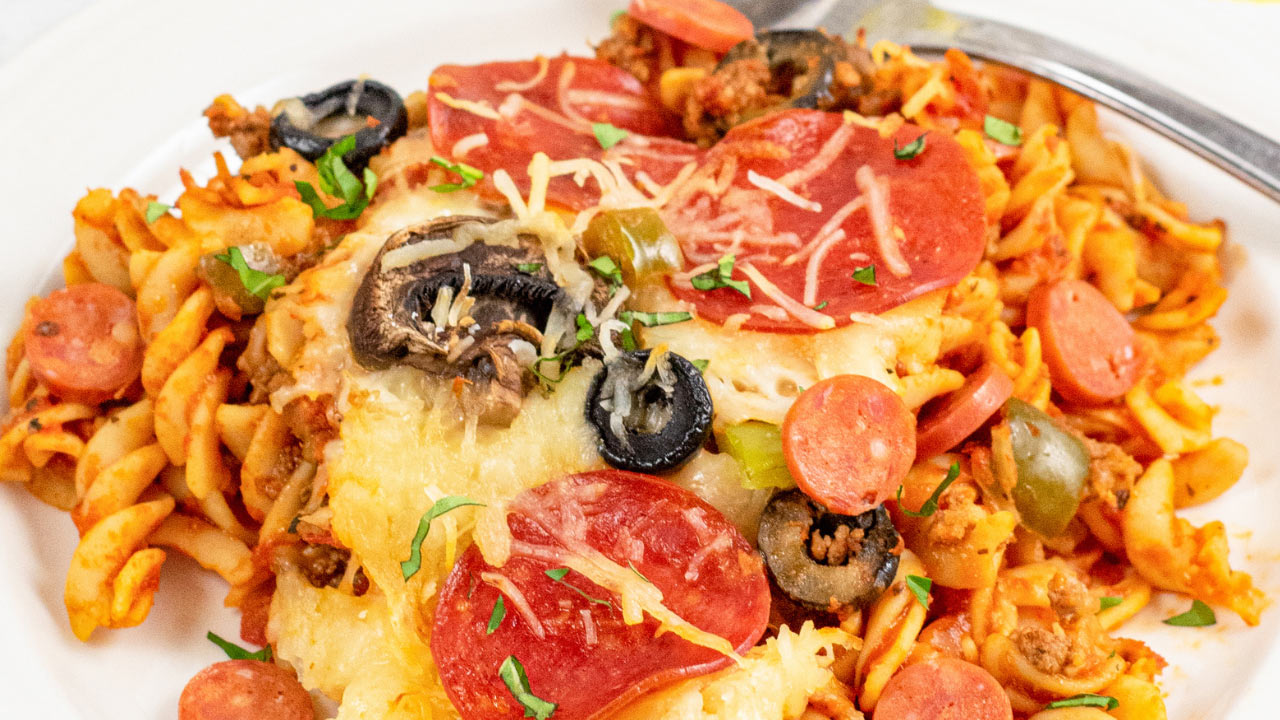 A plate of pasta topped with melted cheese, pepperoni slices, black olives, mushrooms, and green peppers, served with a fork.