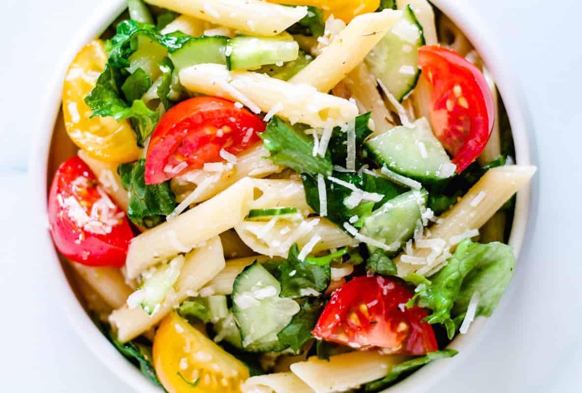 A bowl of pasta salad with penne, sliced cucumbers, cherry tomatoes, lettuce, and grated cheese.