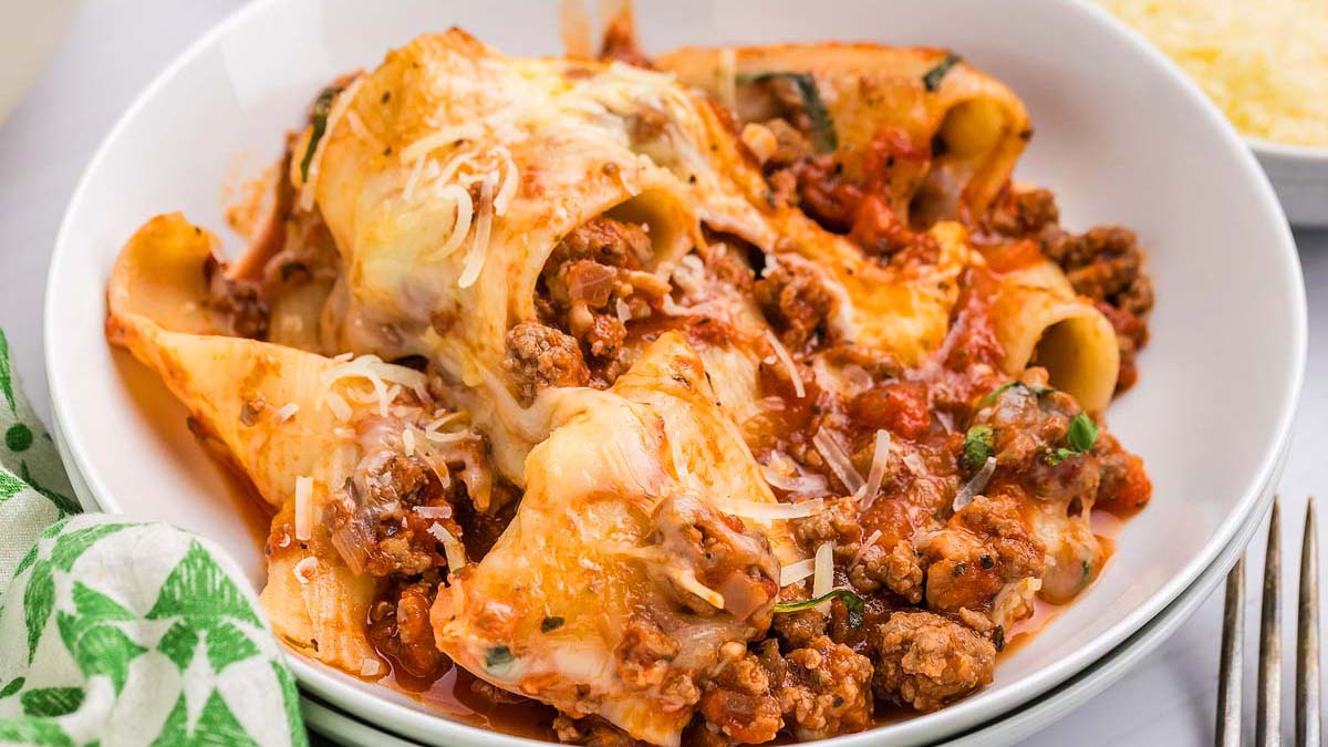 A plate of baked pasta shells filled with ground meat, covered in tomato sauce and melted cheese, garnished with herbs.
