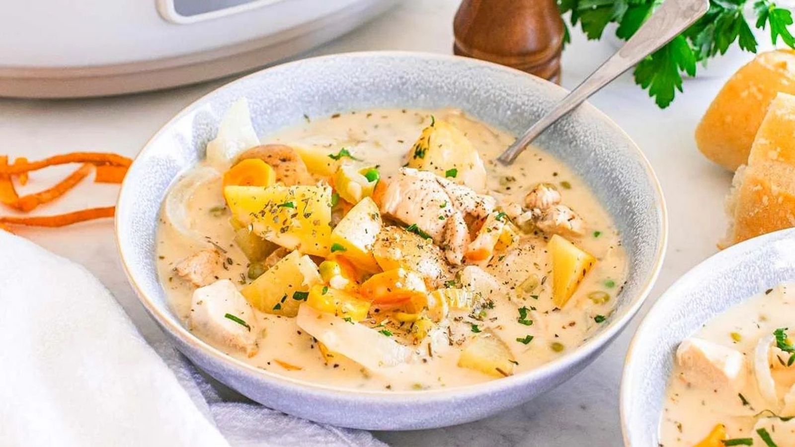 A bowl of creamy chicken stew with chunks of chicken, potatoes, carrots, and herbs, served with a spoon.