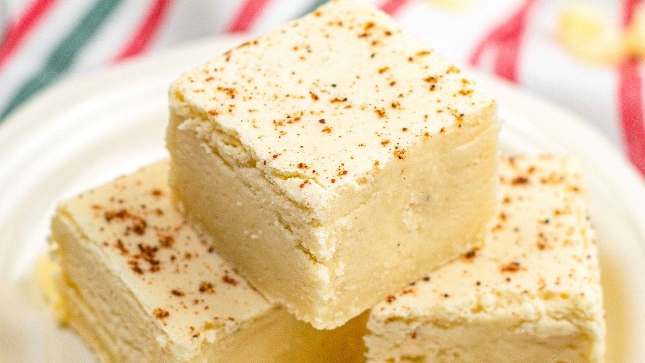 Three square pieces of light-colored fudge with a dusting of spice on top, stacked on a white plate.