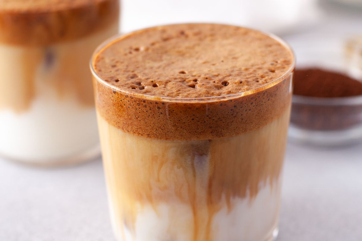 A glass of dalgona coffee with whipped coffee on top of iced milk, showing distinct layers.