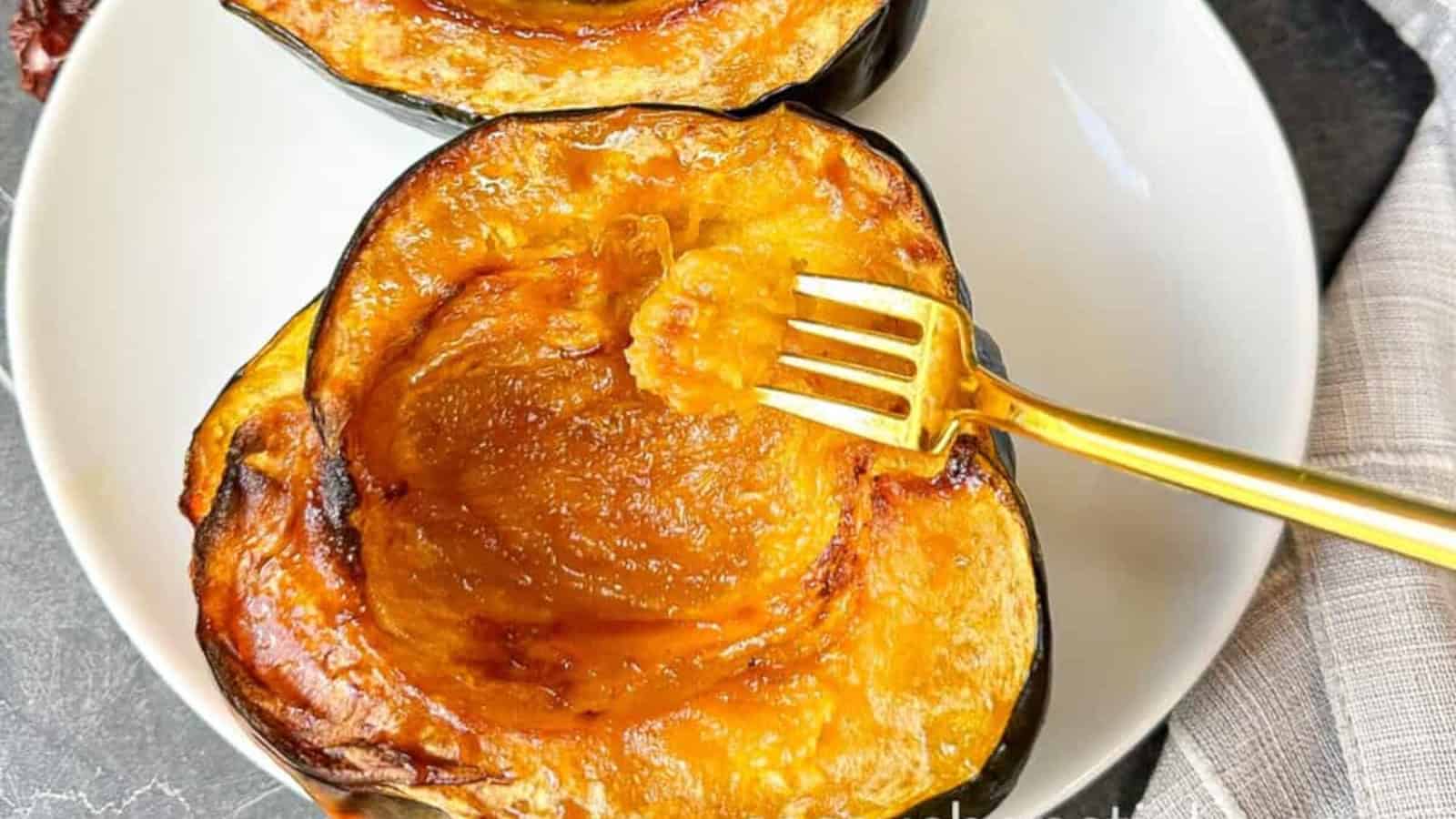 A white plate with two halves of baked acorn squash, one being scooped with a gold fork.