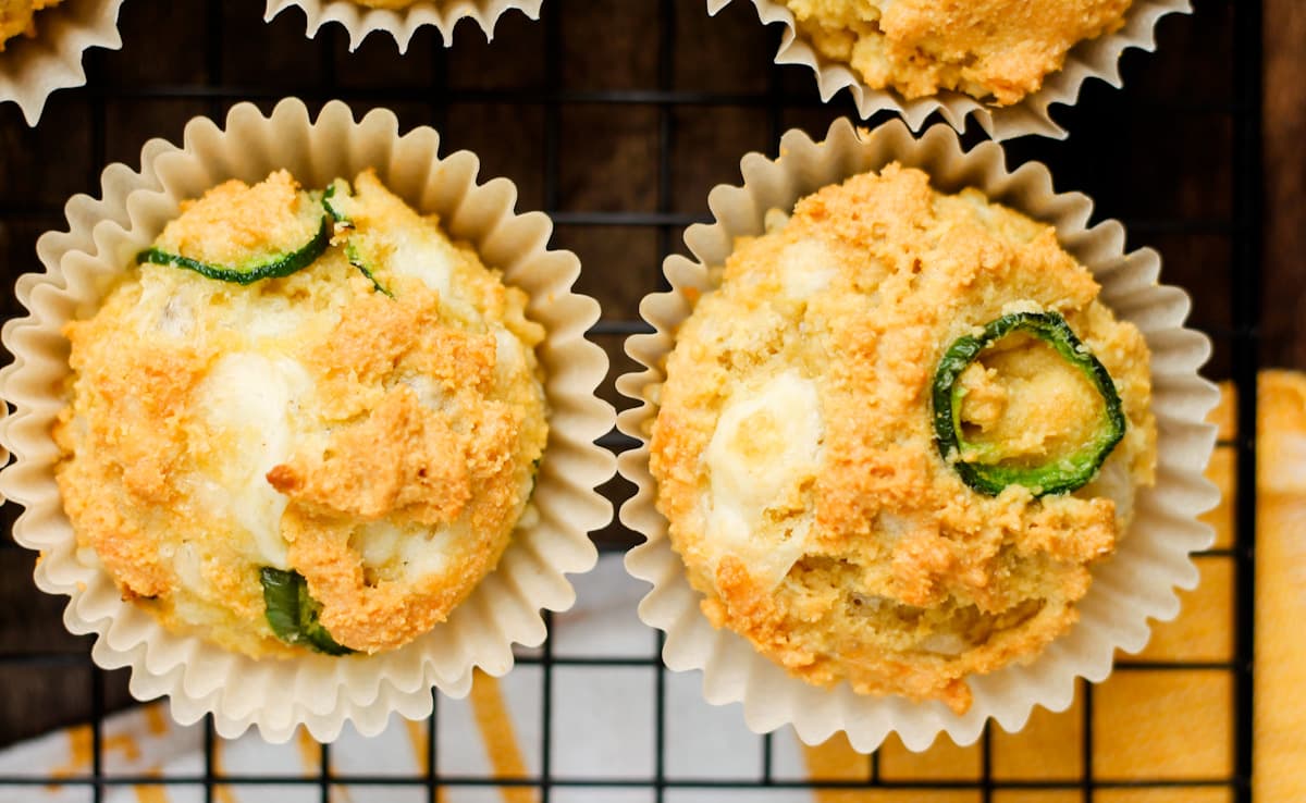 Two savory muffins in paper liners on a cooling rack, topped with sliced green peppers and visible chunks of cheese.