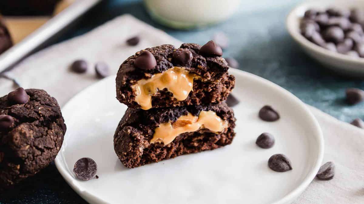 A chocolate cookie broken in half to reveal a creamy peanut butter filling, placed on a white plate with scattered chocolate chips.