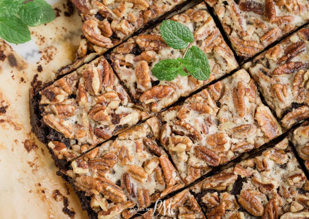 Close-up of sliced pecan bars with a crumbly topping, garnished with fresh mint leaves on parchment paper.