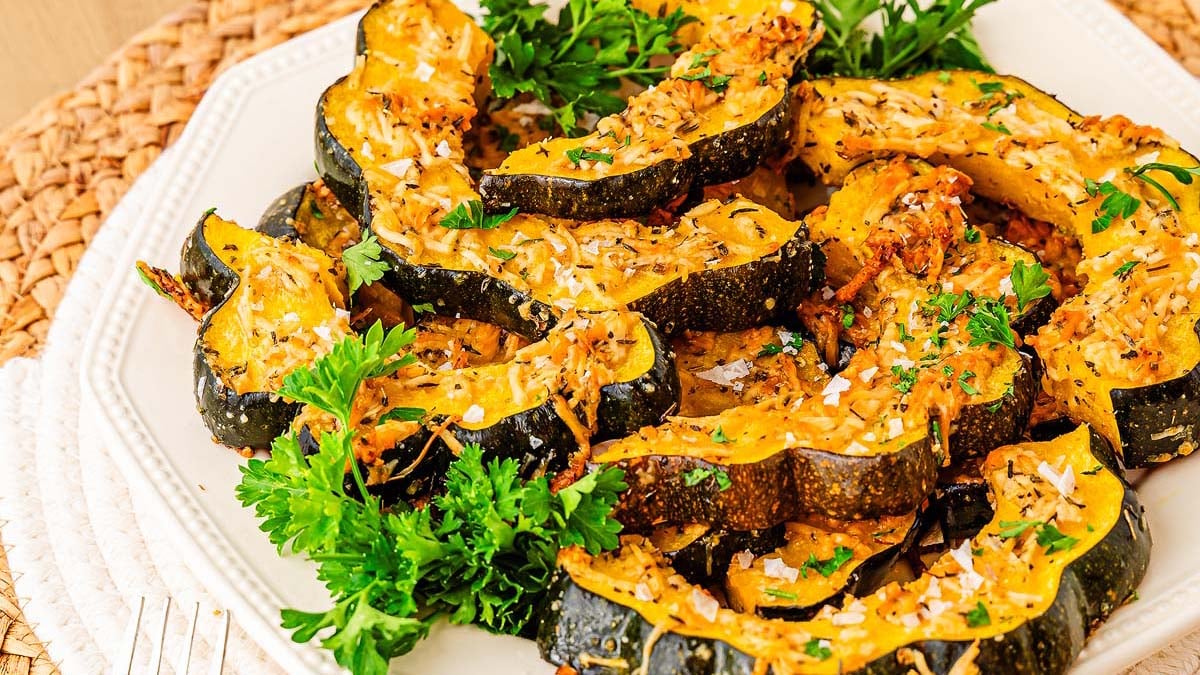 A plate of roasted acorn squash slices garnished with chopped parsley and shredded cheese, served on a white dish.