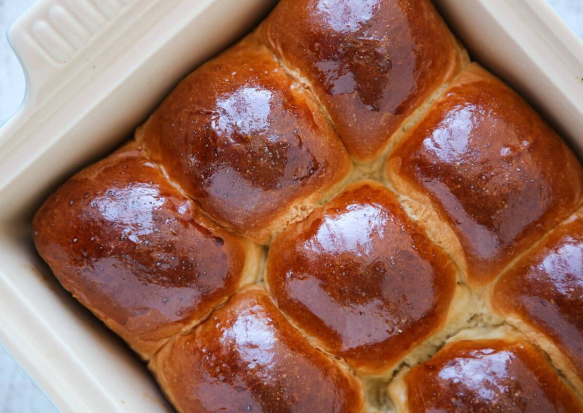 A close-up view of a baking dish containing six shiny, golden-brown bread rolls arranged in two rows.