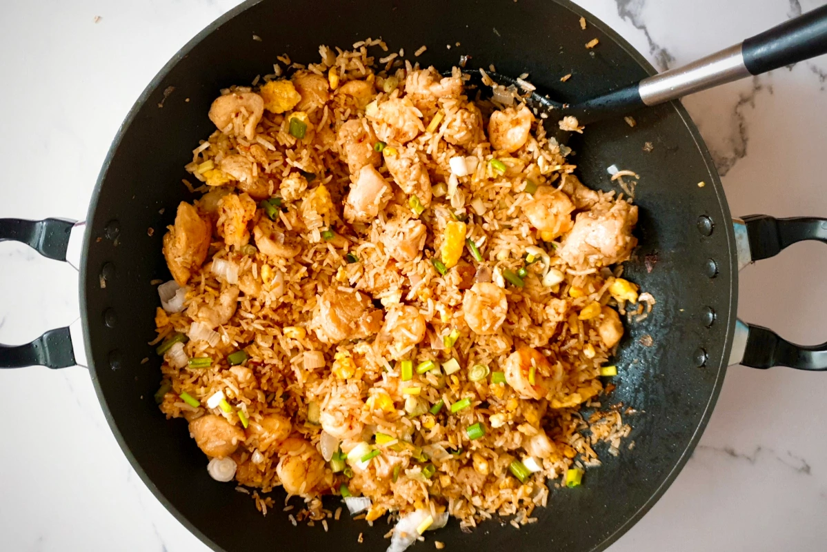 A wok filled with cooked chicken fried rice, including chunks of chicken, fried rice, green onions, and eggs, with a serving spoon resting inside.