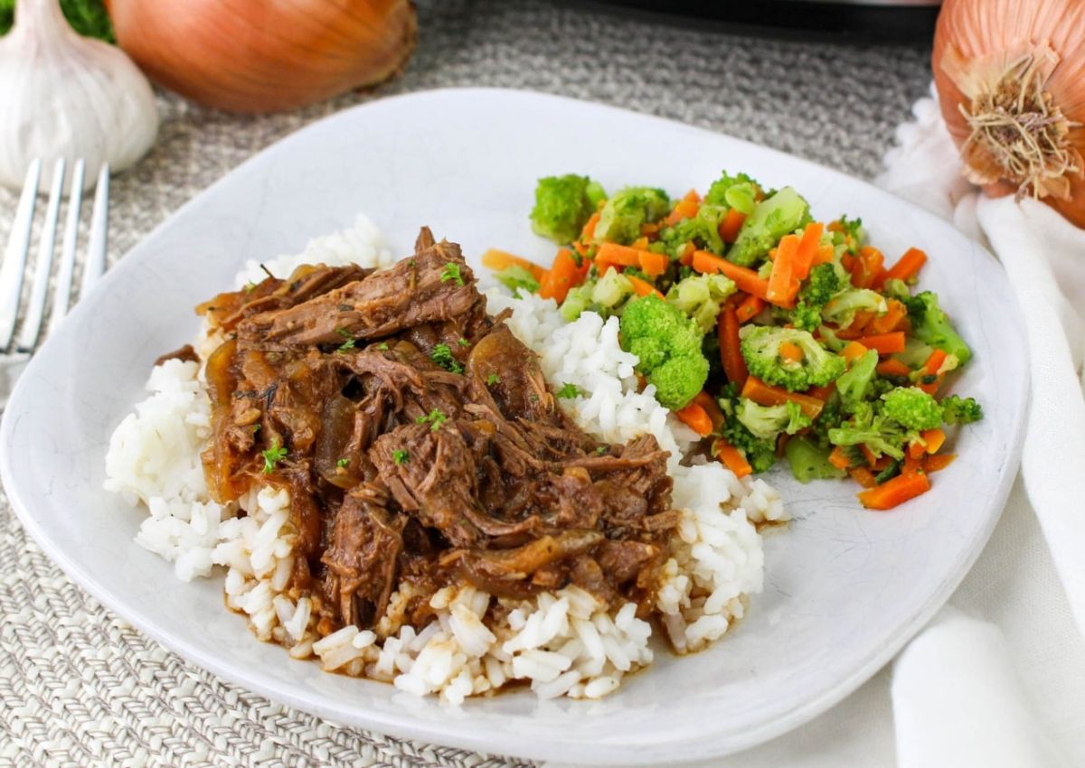 A plate with shredded beef in sauce over white rice, served with a side of mixed vegetables including broccoli and carrots.