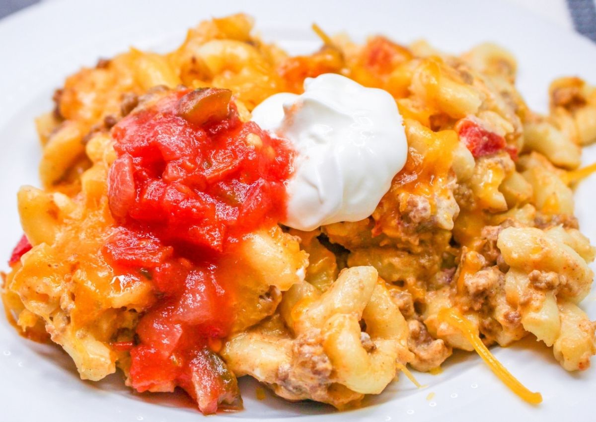 A plate of cheesy macaroni casserole with ground beef, topped with salsa and a dollop of sour cream.