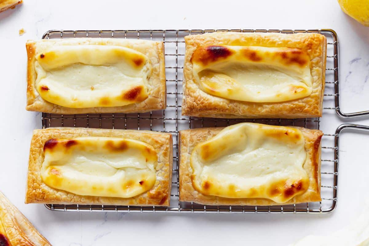 Four rectangular cheese danishes with golden-brown edges and creamy cheese filling cooling on a wire rack.
