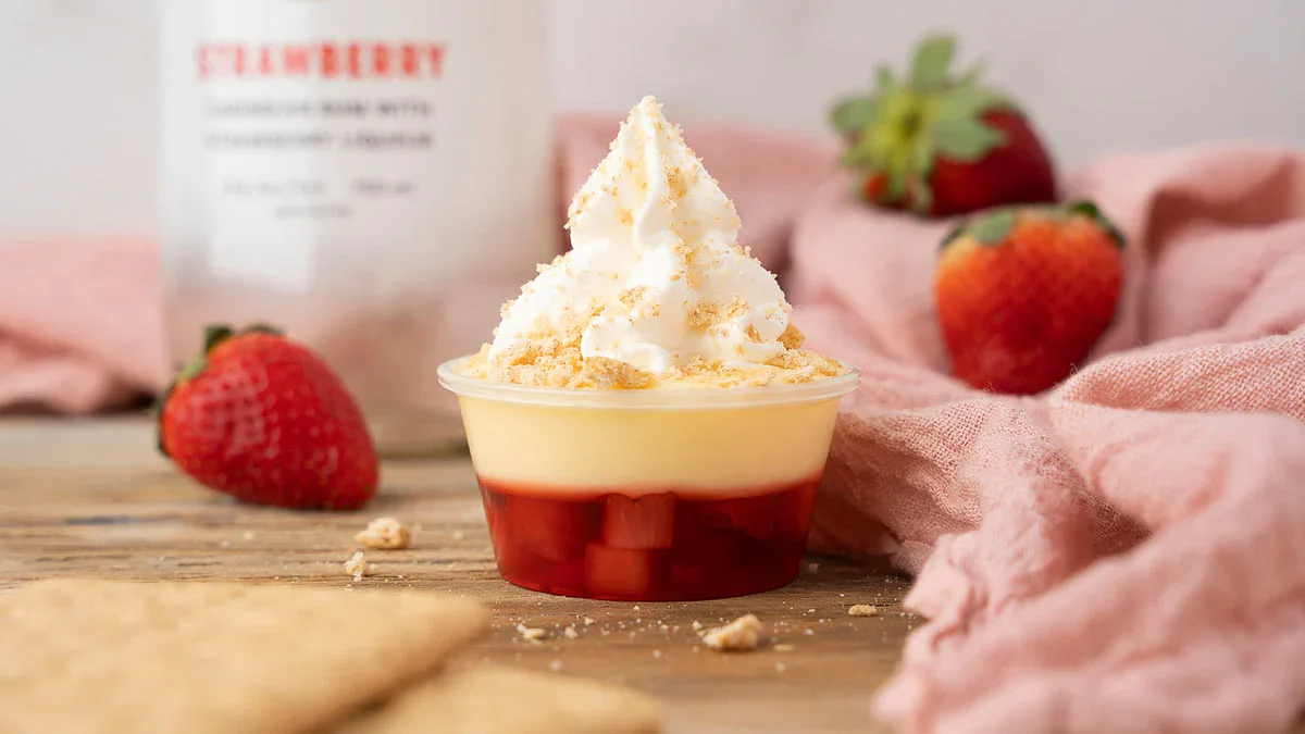 A small dessert cup with whipped topping, crumbled cookie, yellow custard, and strawberry filling, with fresh strawberries and graham crackers in the background.