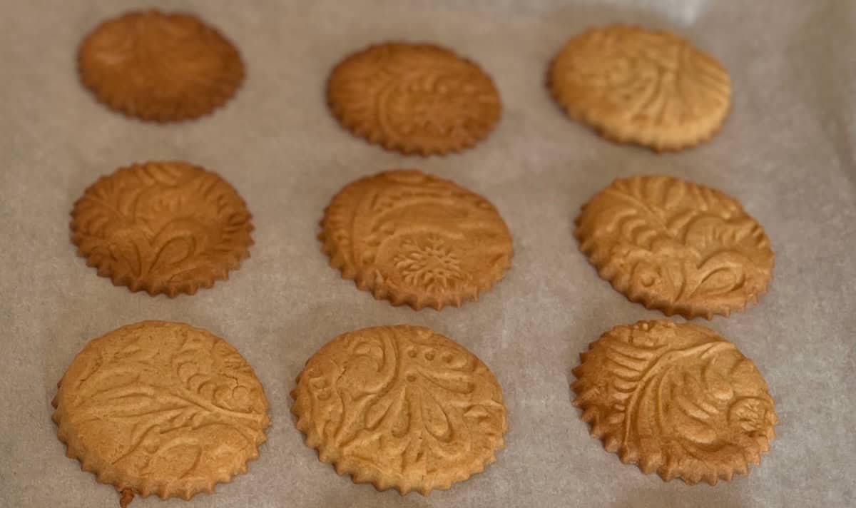 Nine embossed round cookies with decorative patterns are arranged in three rows on a parchment-lined baking tray.