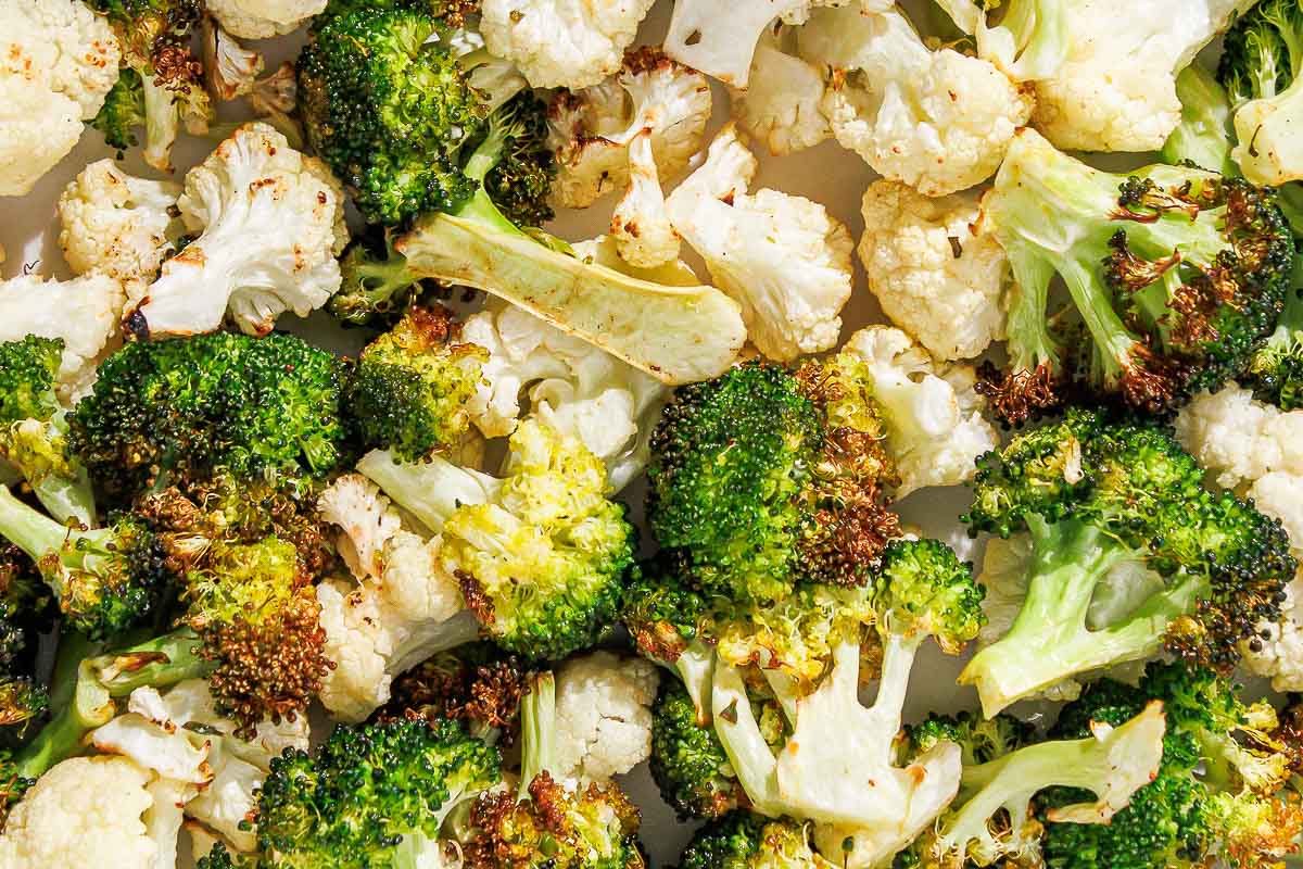 Close-up of roasted broccoli and cauliflower florets with browned, crispy edges on a baking sheet.