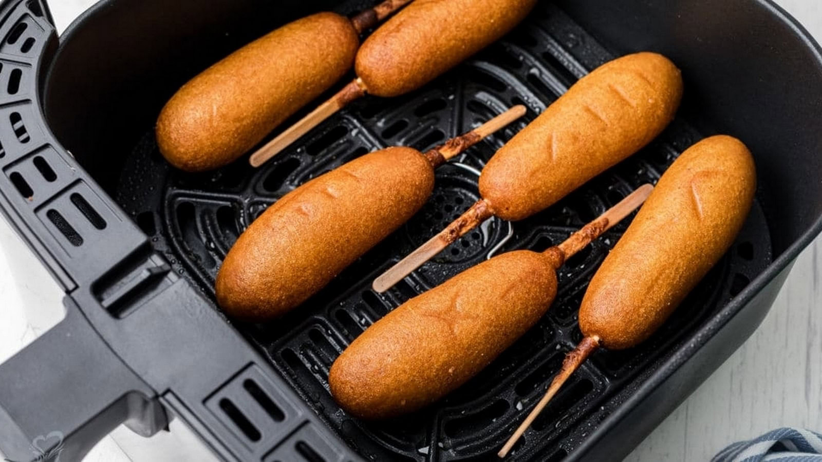 Five corn dogs on sticks are arranged inside the basket of an air fryer, ready to be cooked or recently cooked.
