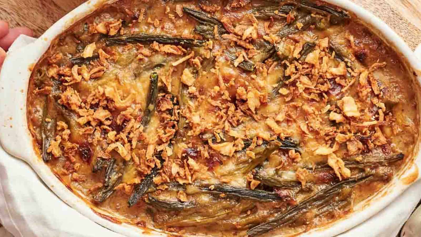 A baked green bean casserole topped with crispy fried onions in a white oval dish.