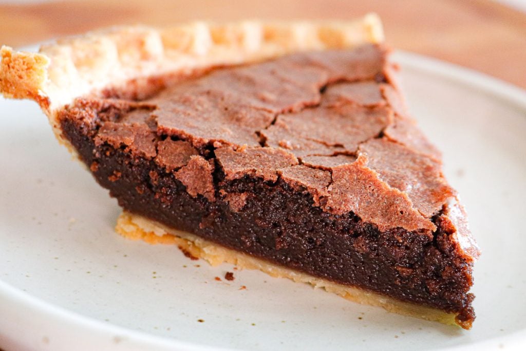 A slice of chocolate chess pie with a flaky crust on a white plate.