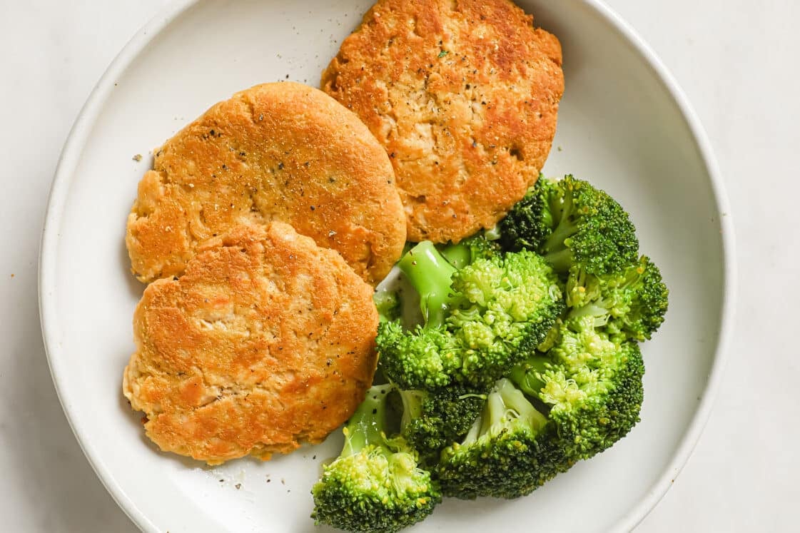 A white plate with three golden-brown patties and a serving of steamed broccoli.