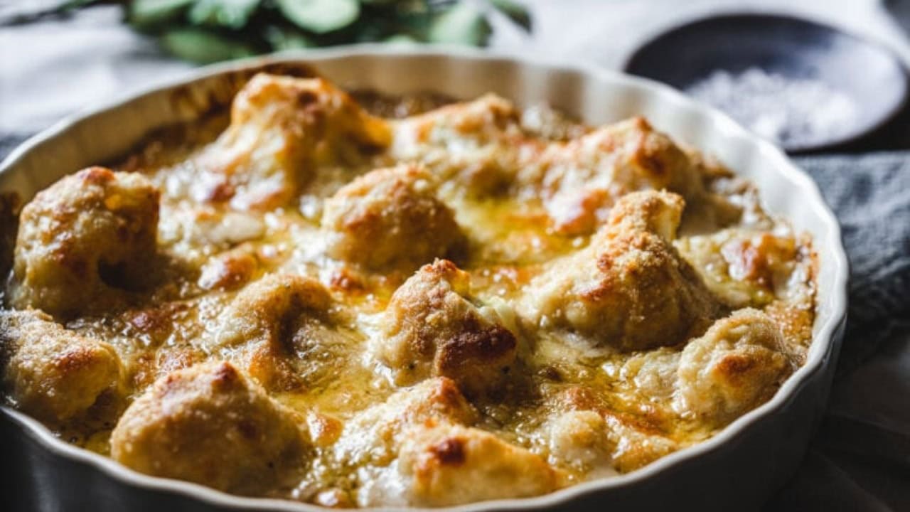 A baked dish in a round white pan features golden brown, cheese-covered cauliflower florets.