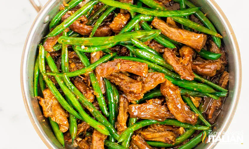 A skillet filled with cooked green beans and sliced beef in a brown sauce.