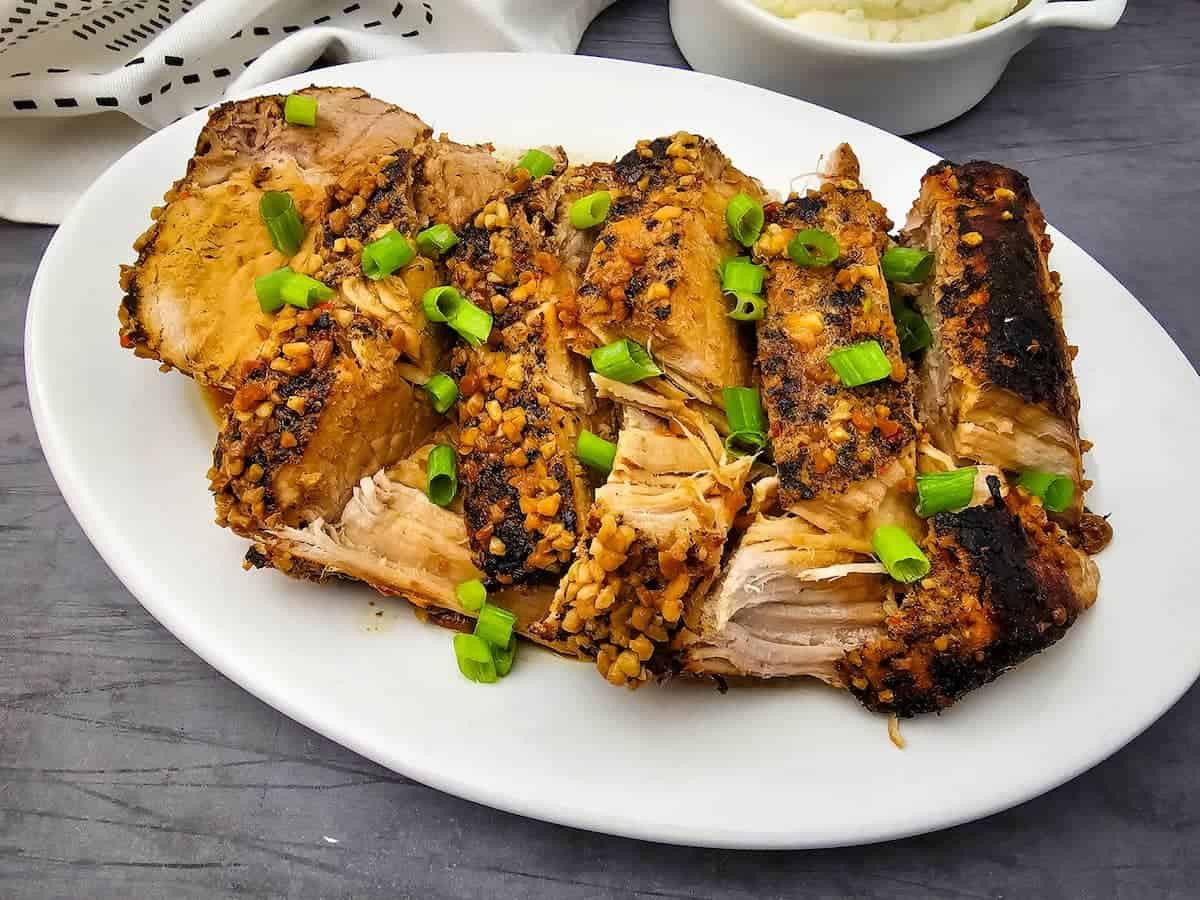 Sliced roasted pork with a garlic and herb crust, garnished with chopped green onions, served on a white plate.