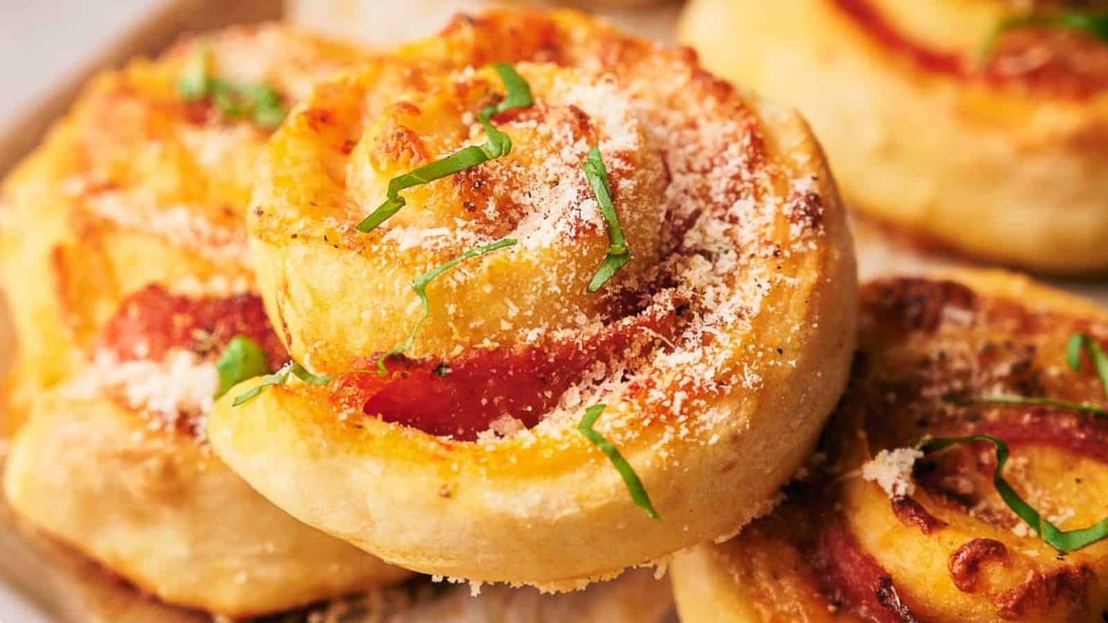 Close-up of pizza rolls topped with grated cheese and fresh basil, showing golden, baked dough with visible tomato sauce and melted cheese.