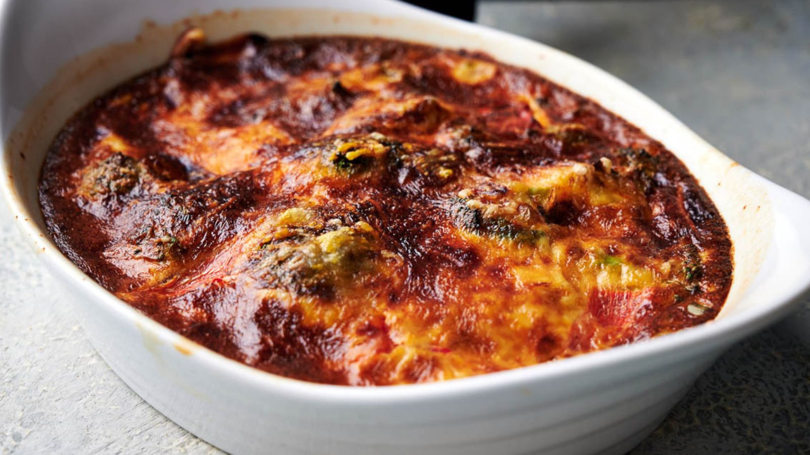 A baked casserole dish filled with browned, cheesy stuffed shells covered in marinara sauce sits on a light surface.