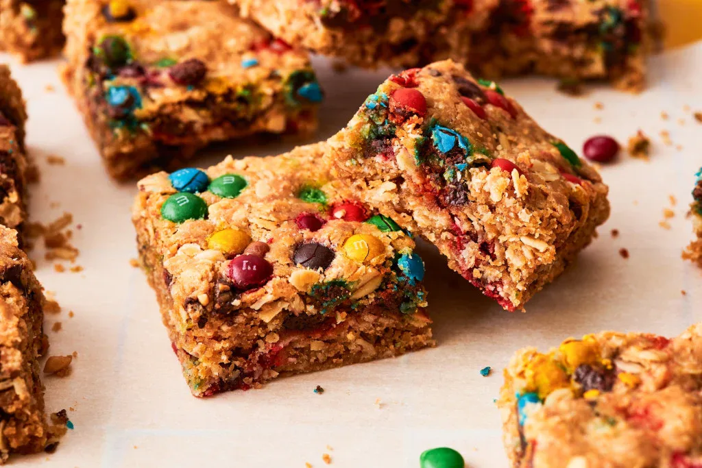 Close-up of homemade cookie bars with oats and colorful chocolate candies on a sheet of parchment paper.