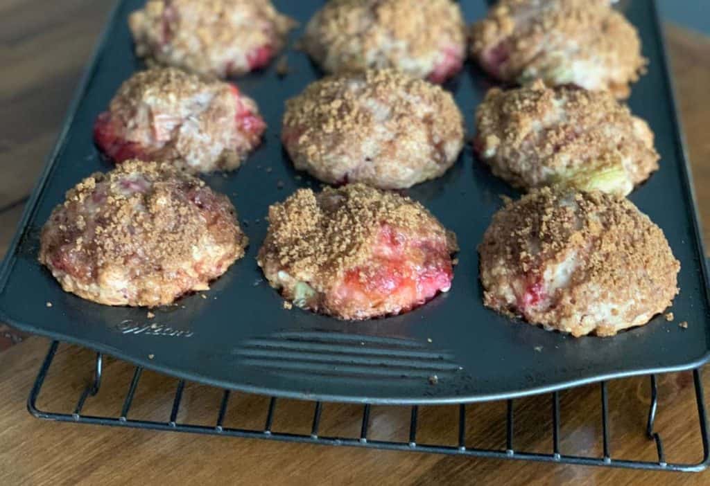 Nine fruit-filled muffins with a crumb topping sit in a non-stick muffin pan, cooling on a wire rack on a wooden surface.