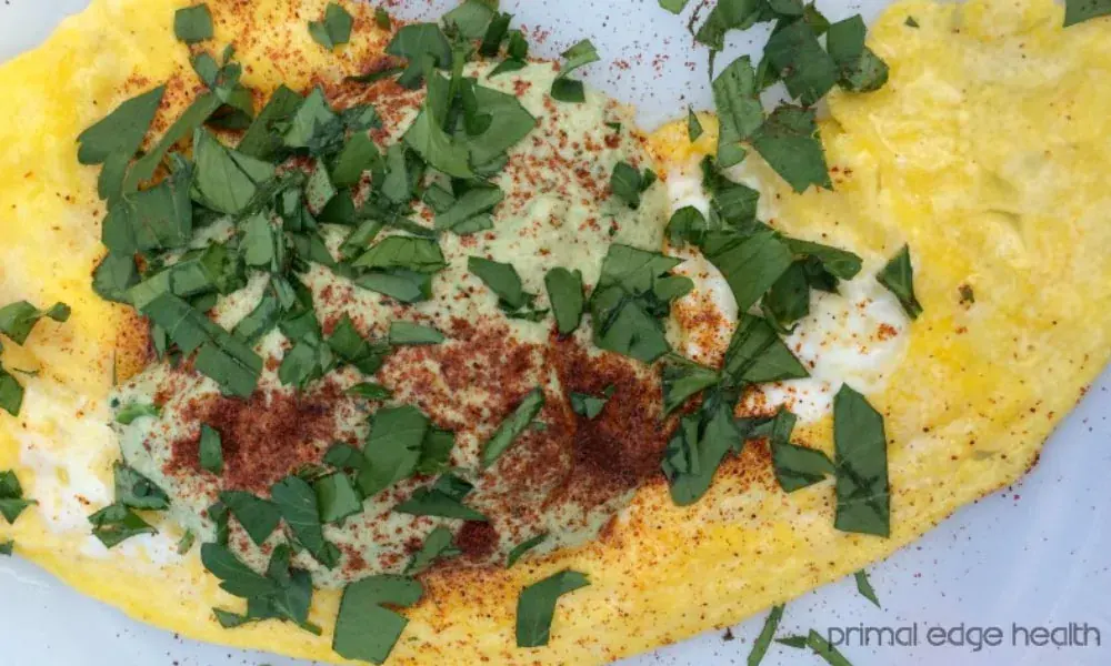 Omelet topped with green herbs, creamy sauce, and sprinkled paprika on a white plate.