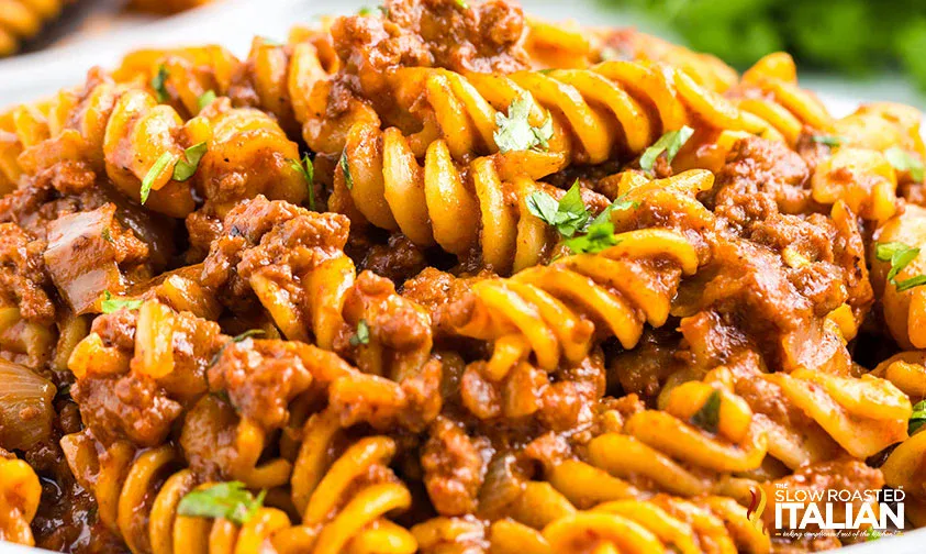 Close-up of rotini pasta mixed with ground beef and tomato sauce, garnished with chopped parsley.
