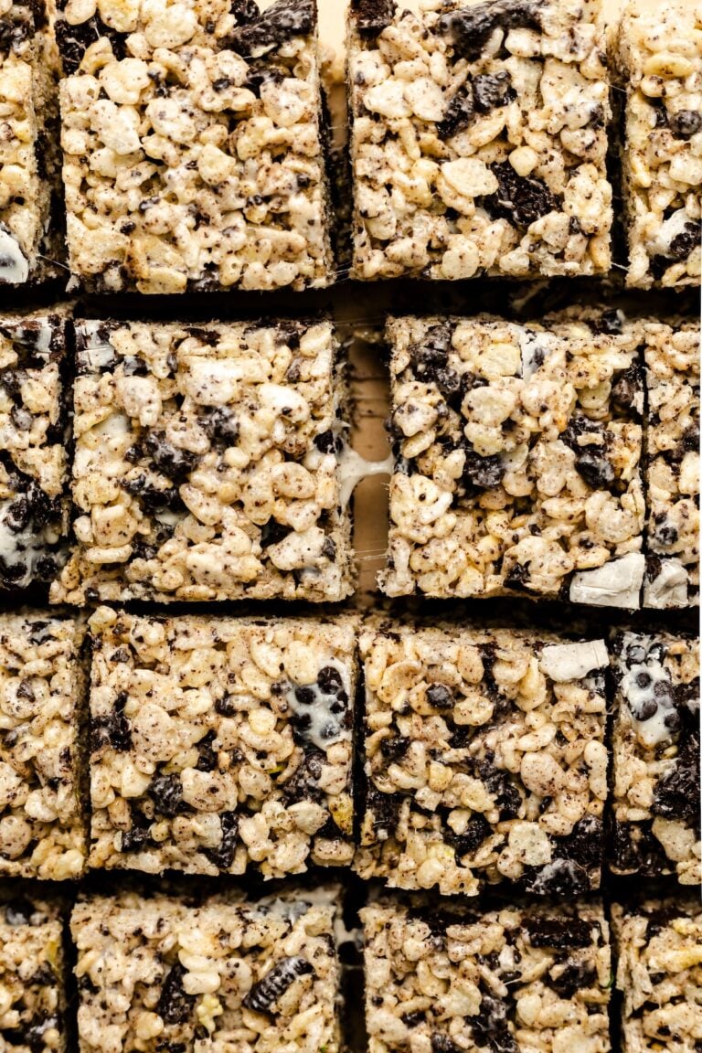 Close-up of evenly cut rice crispy treats mixed with crushed cookies and marshmallows, arranged in rows on a parchment-lined surface.