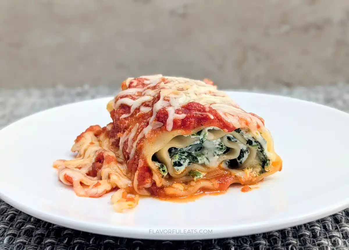 A serving of spinach and ricotta lasagna roll topped with melted cheese and tomato sauce on a white plate.