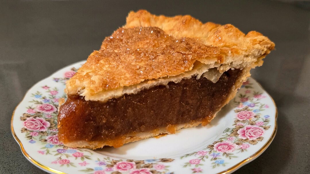 A slice of brown sugar pie with a golden, flaky crust sits on a floral-patterned plate against a dark background.