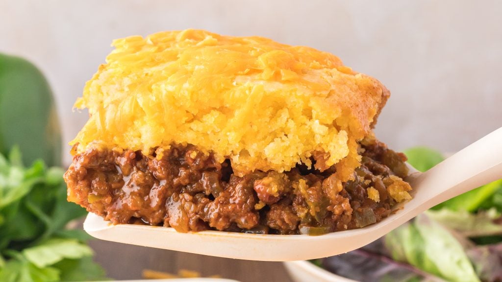 A close-up of a serving of casserole with a layer of ground beef and sauce topped with golden cornbread on a spatula.